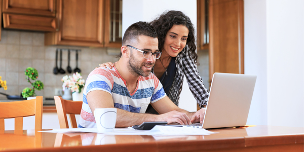 A couple sitting at a table looking at a laptop.